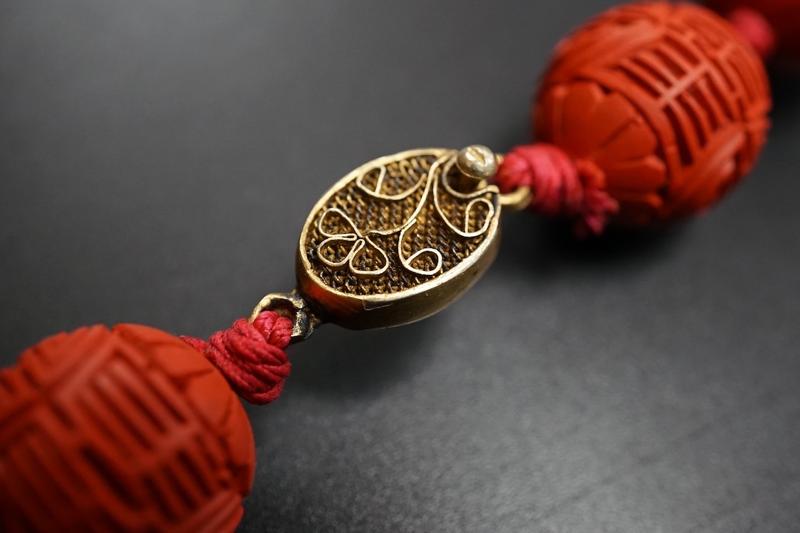 A Chinese red lacquered bead necklace and a bowenite jade figure of a cat